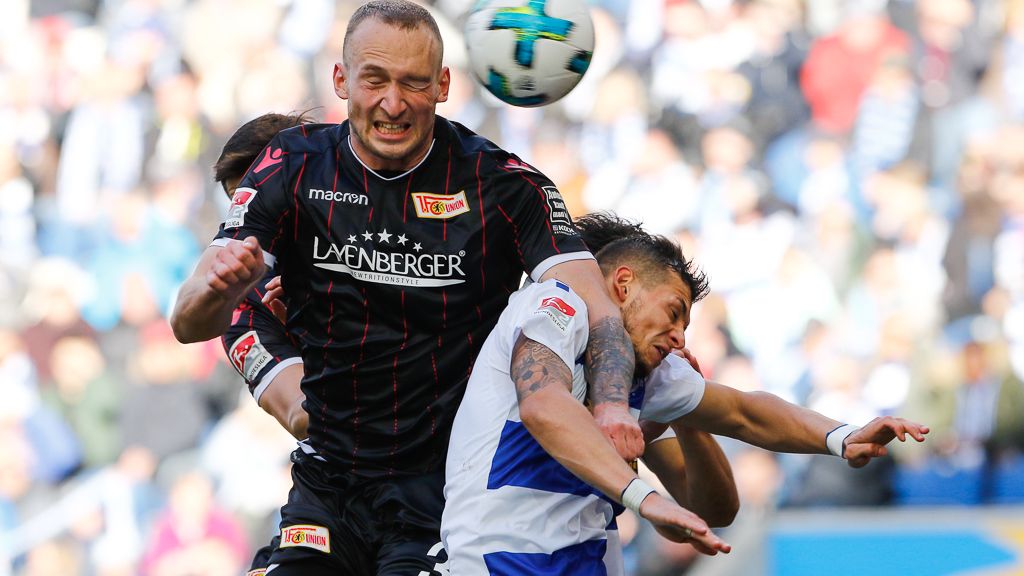 Zwei Fußballspieler geraten während eines Spiels in einen Kopfballduell, der Ball fliegt durchs Bild.