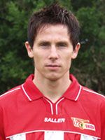 Ein sportlicher Mann mit kurzen, braunen Haaren trägt ein rotes Trikot mit der Aufschrift "FC Union". Hintergrund ist unscharf und grün.