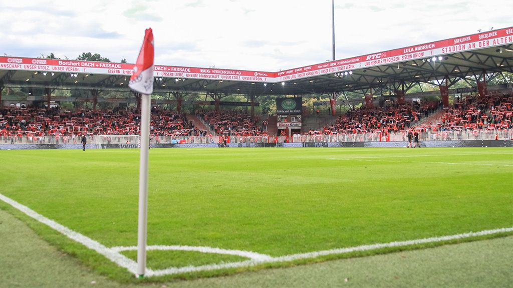 Ein Blick auf ein Fußballstadion mit Rasen, Eckfahne und vielen Zuschauern auf den Tribünen.