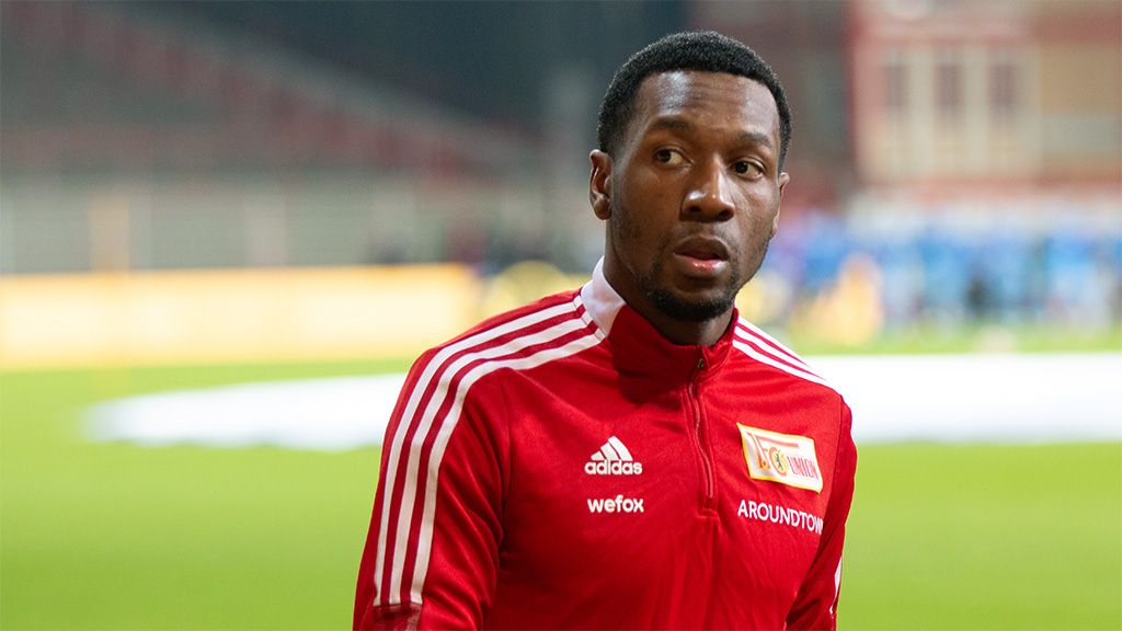 Ein Fußballspieler in rotem Vereinsanzug steht nachdenklich auf dem Spielfeld.