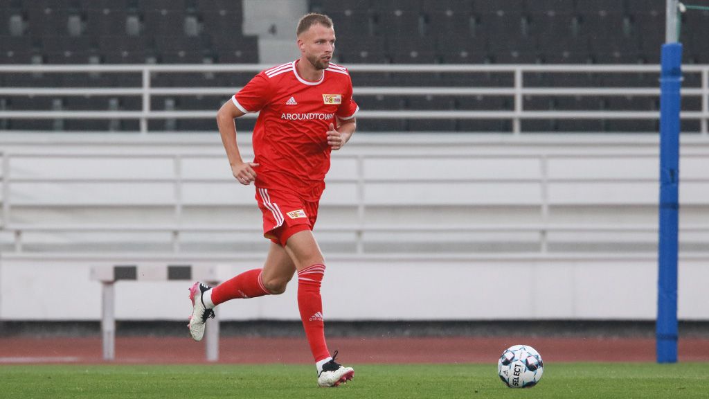 Fußballspieler in rotem Trikot und Shorts läuft auf dem Spielfeld mit einem Ball.