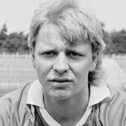 Schwarz-weiß Porträt eines jungen Mannes mit blonden, leicht zerzausten Haaren, der direkt in die Kamera schaut.