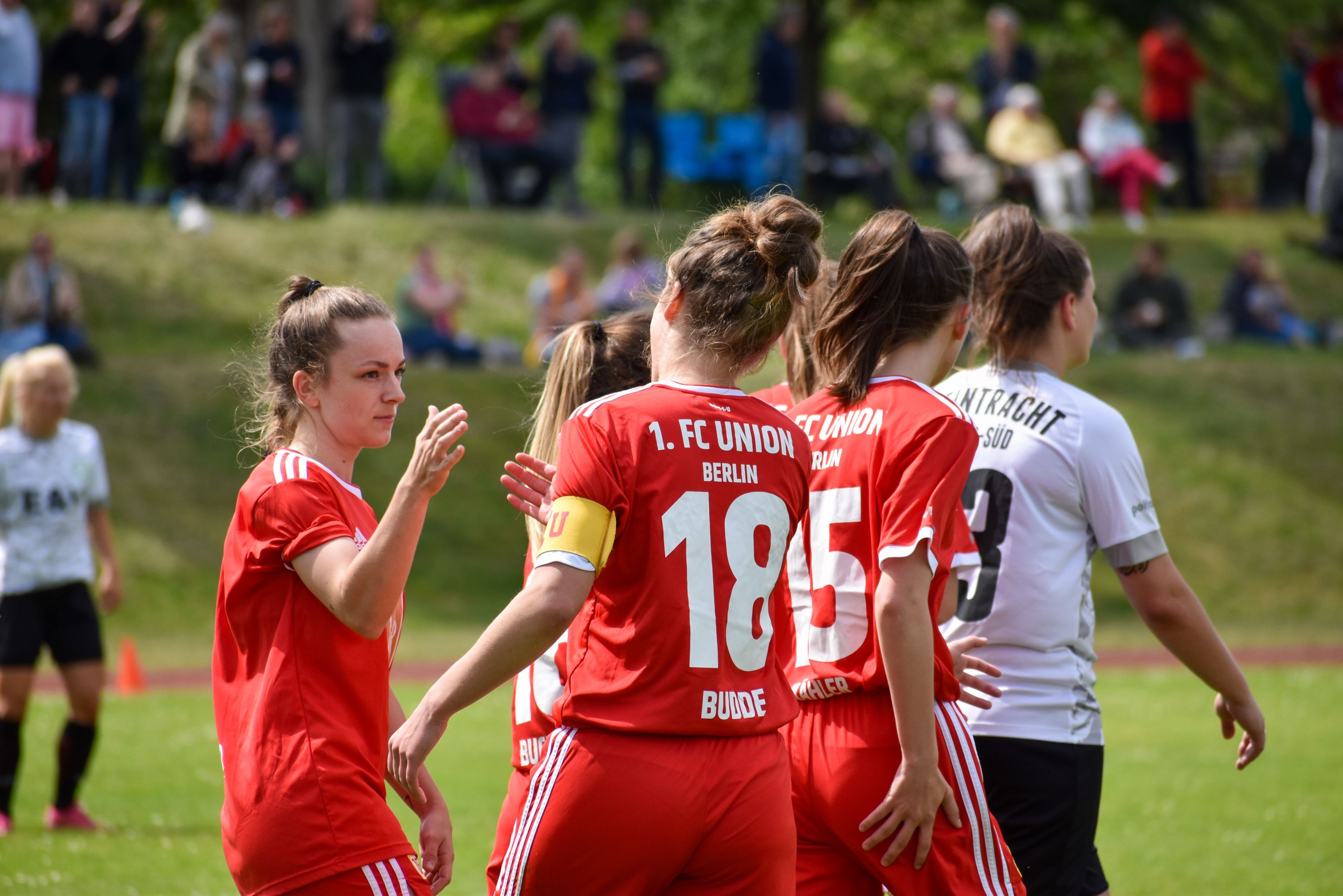 Die Spielerinnen vom 1. FC Union Berlin stehen auf dem Platz. Sie tragen rot-weiße Trikots. Sie grüßen sich nach einem Spielzug.