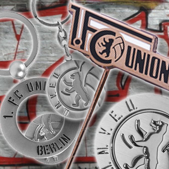Verschiedene Schlüsselanhänger und Pins des 1. FC Union Berlin, abgebildet vor einer graffitibesprühten Wand.