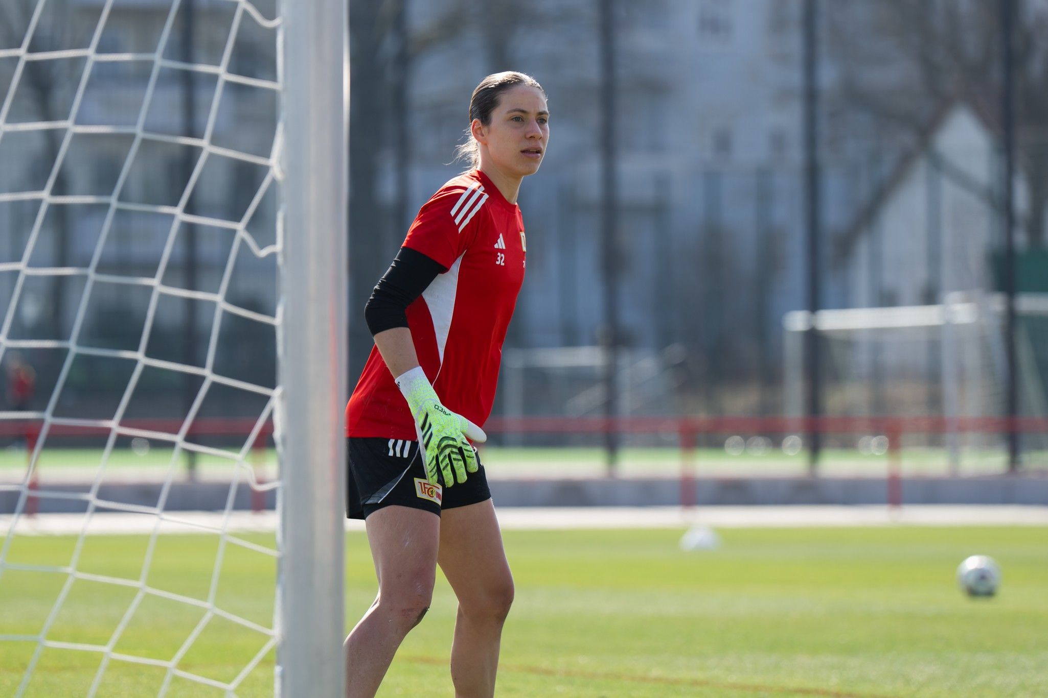 Torhüterin in rot-weißem Trikot und Handschuhen steht im Tor während des Trainings auf einem Fußballfeld.