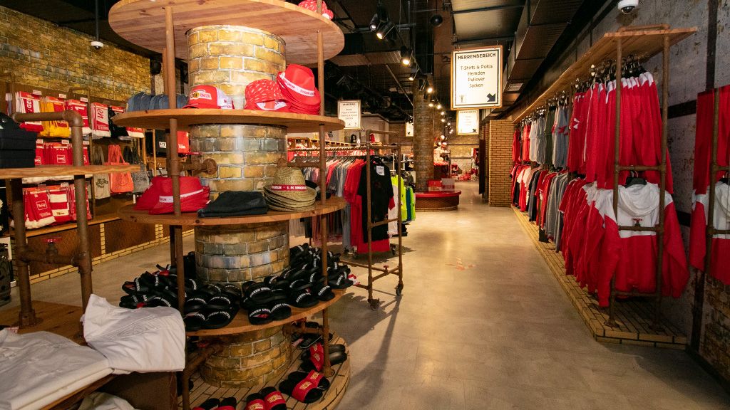 Ein Einzelhandelsgeschäft mit Kleidung in Rot- und Schwarztönen, Regalen und einer zentralen Säule mit Schuhen und Accessoires.