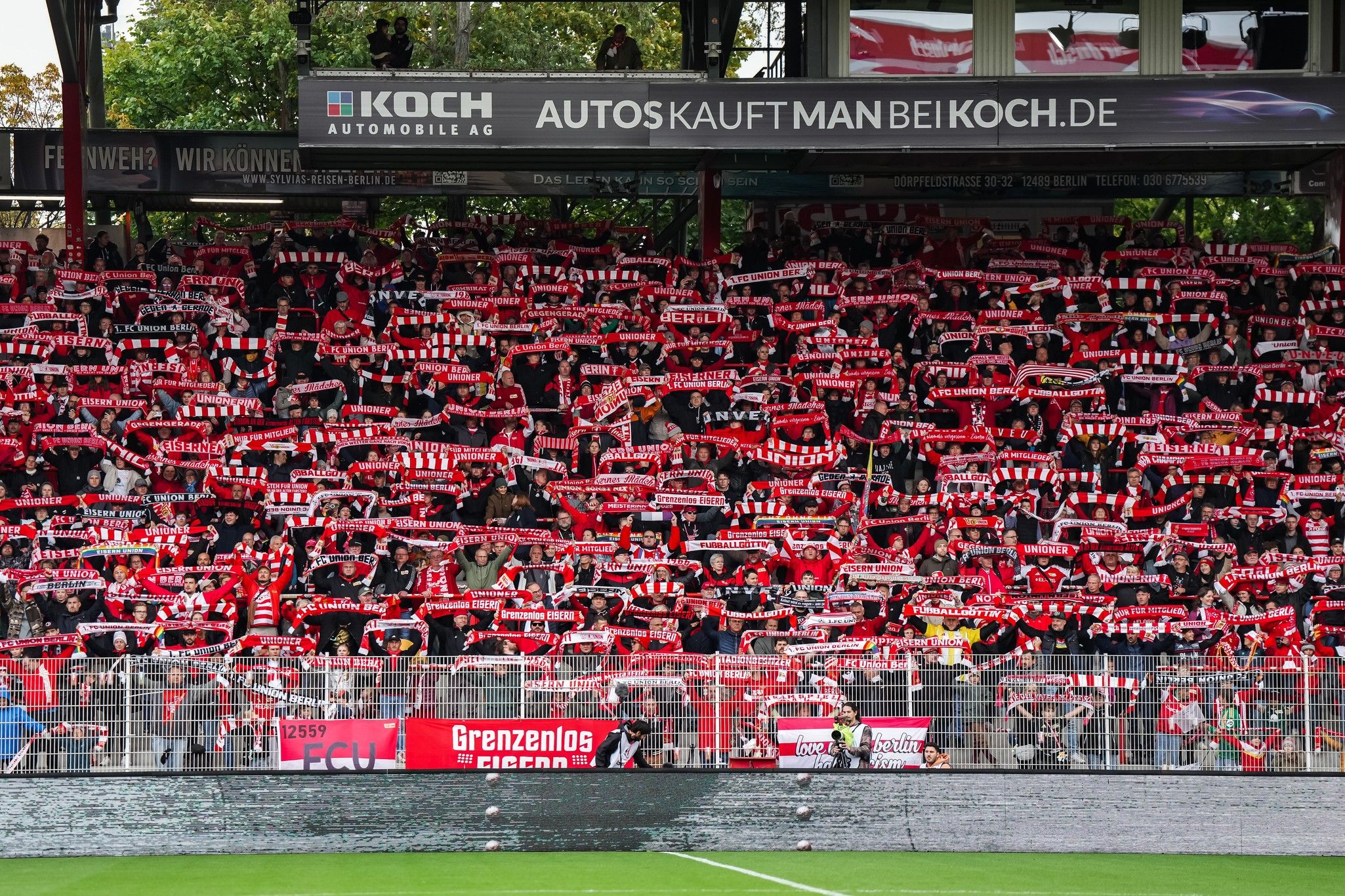 Eine große Menge von Fans mit roten Schals in einem Stadion, die leidenschaftlich ihr Team unterstützen.