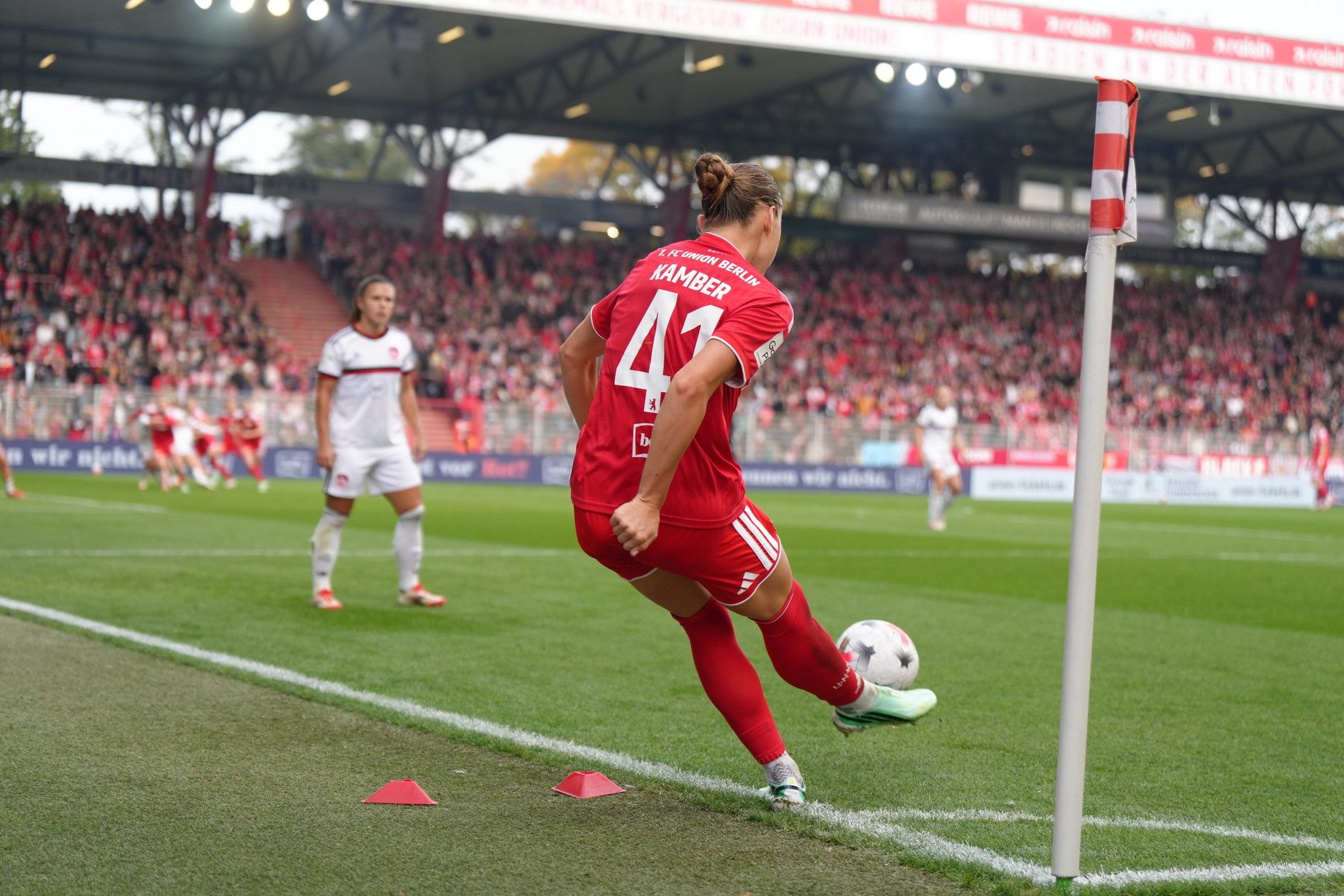 Fußballspieler führt einen Eckstoß aus, umgeben von Zuschauern im Stadion und seinen Mitspielern.