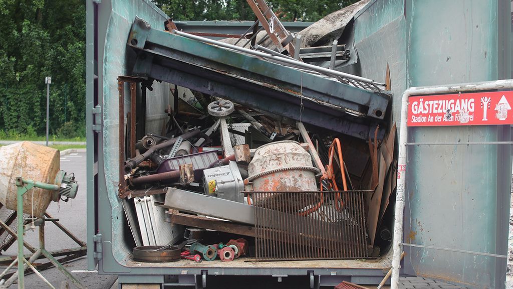 Voller Container mit verschiedenen Metall- und Abfallgegenständen, darunter Rohre, Maschinen und Bauzubehör.