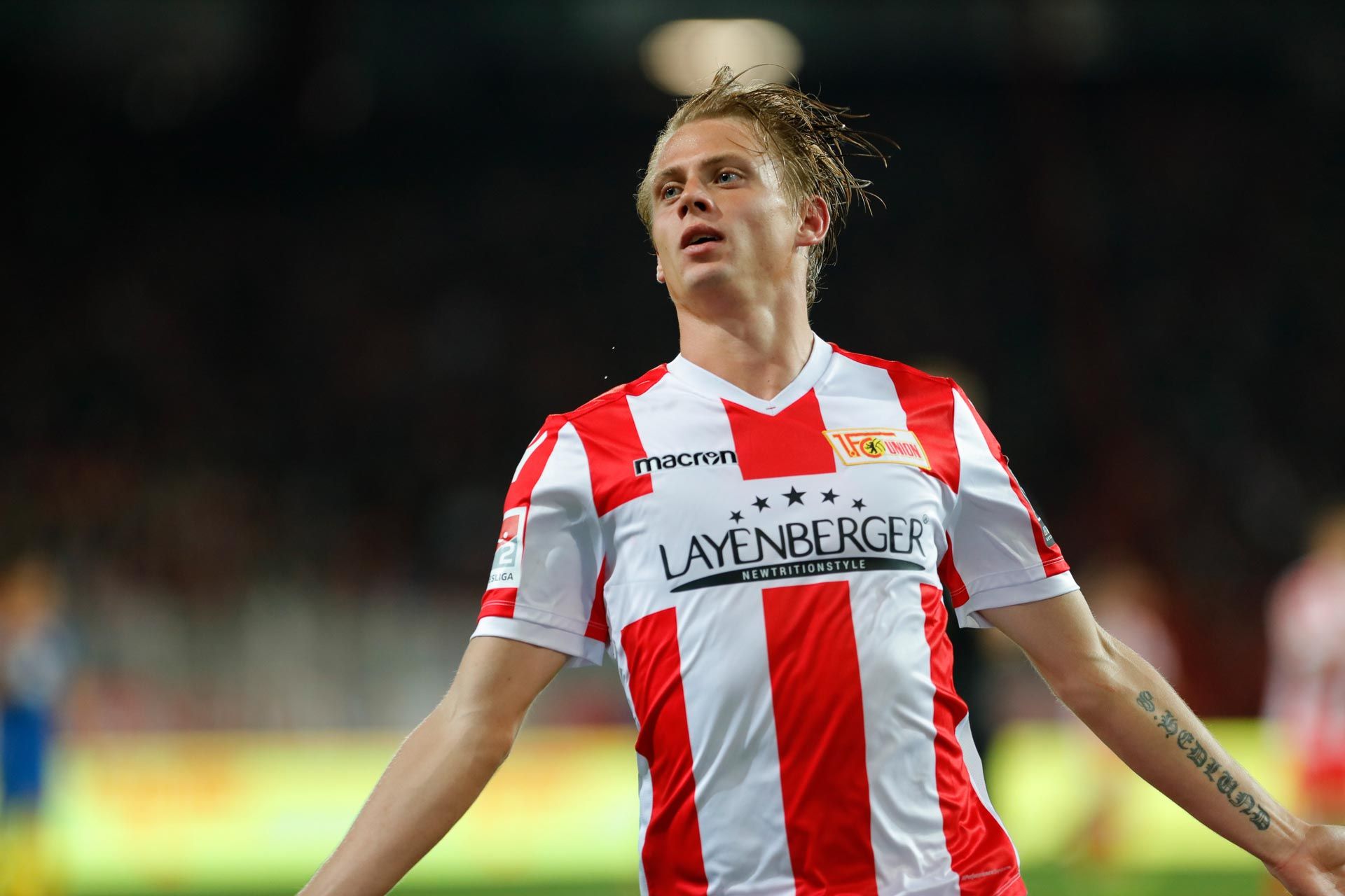 Ein Fußballspieler trägt ein rot-weiß gestreiftes Trikot. Er hat aufgestellte Haare. Er freut sich nach dem Spiel.