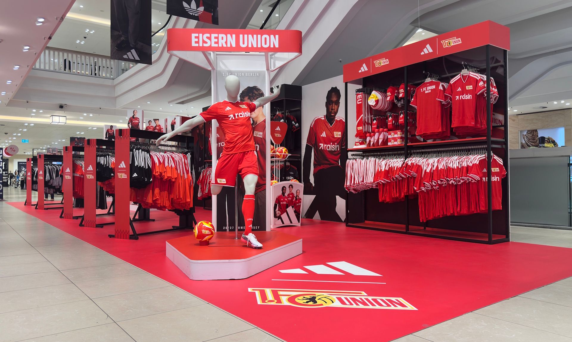 Schaufenster mit rot-weißer Fußballbekleidung von EISERN UNION, inklusive Mannequin und Regalen voller Trikots und Fanartikel.