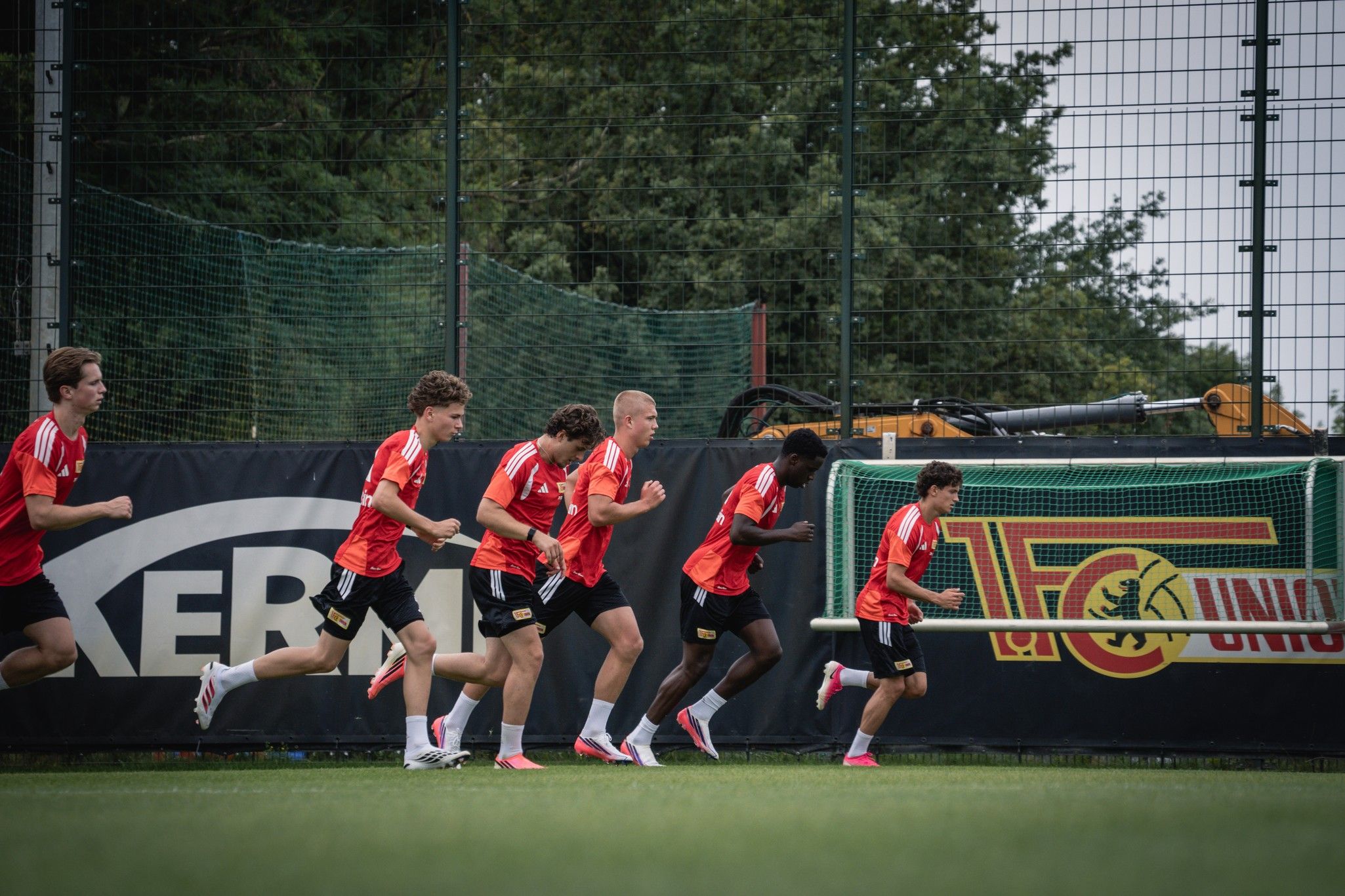 Sechs junge Fußballspieler in roten Trikots laufen auf einem Trainingsplatz.