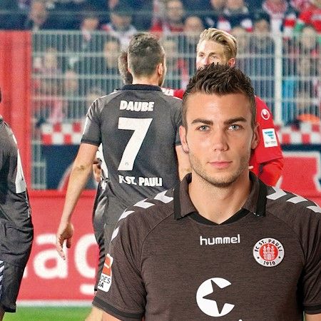 Ein Fußballspieler in einem grauen Trikot steht im Vordergrund, während andere Spieler im Hintergrund agieren.