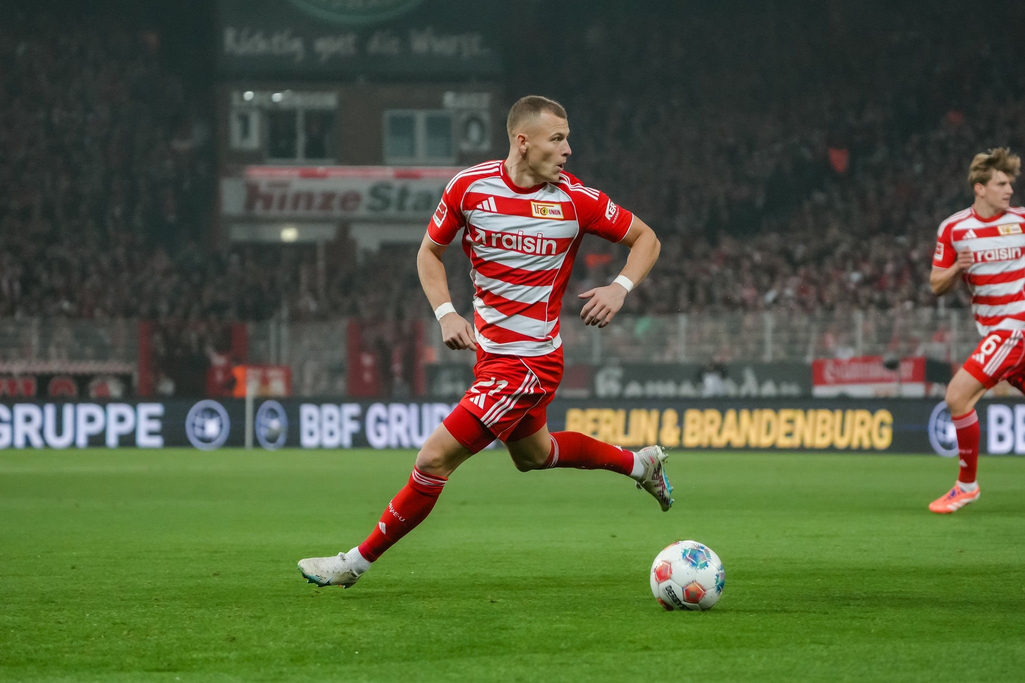 Ein Spieler in rot-weiß gestreiftem Trikot sprintet über das Spielfeld, mit einem Publikum im Hintergrund.