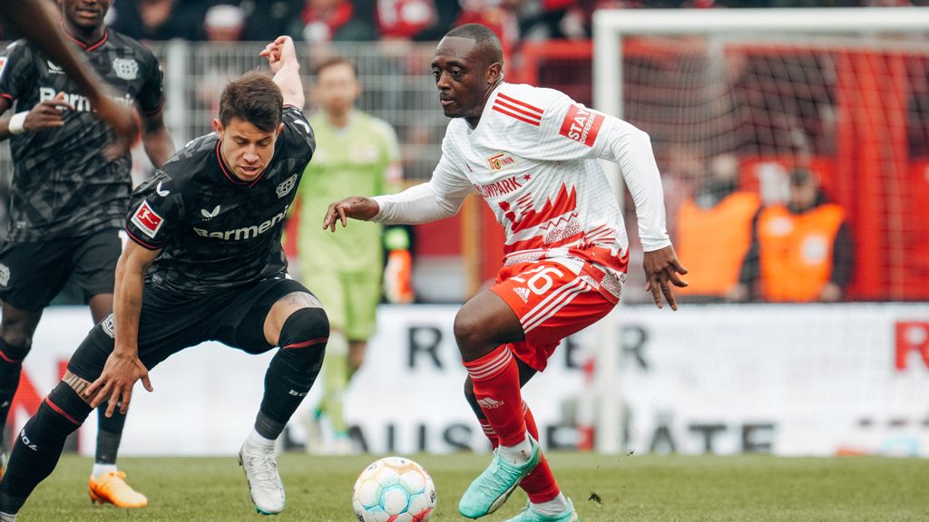 Two football players during a match, one in a black jersey and the other in a red and white jersey, in action.