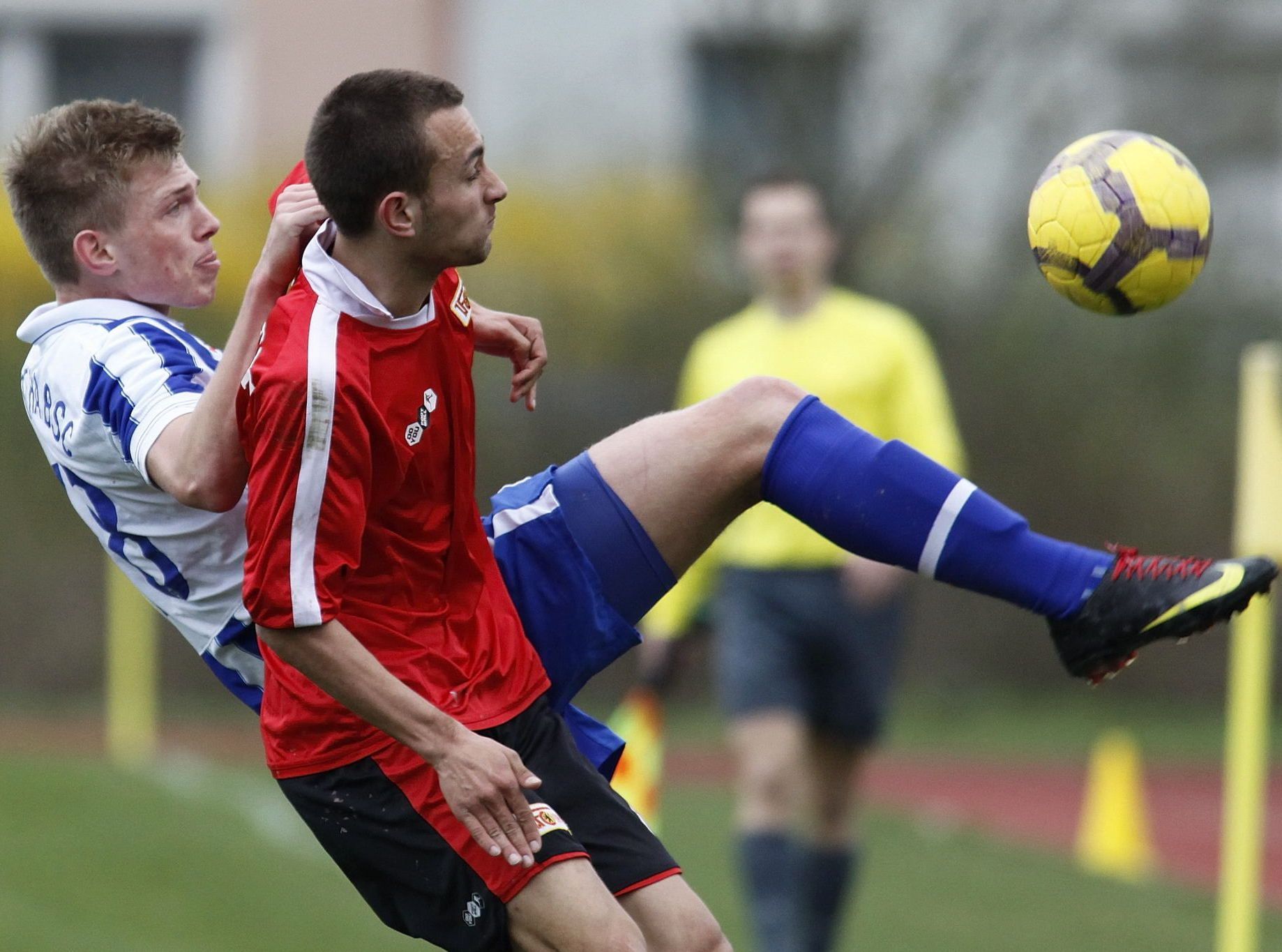 Zwei Fußballspieler in einer intensiven Spielsituation, einer hebt den anderen während eines Zweikampfs an.