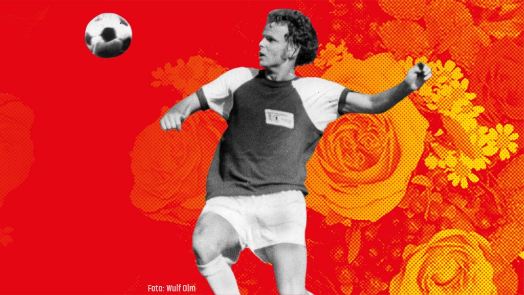 Ein Fußballspieler in Aktion, der einen Ball kickt, vor einem leuchtend roten und floral gemusterten Hintergrund.