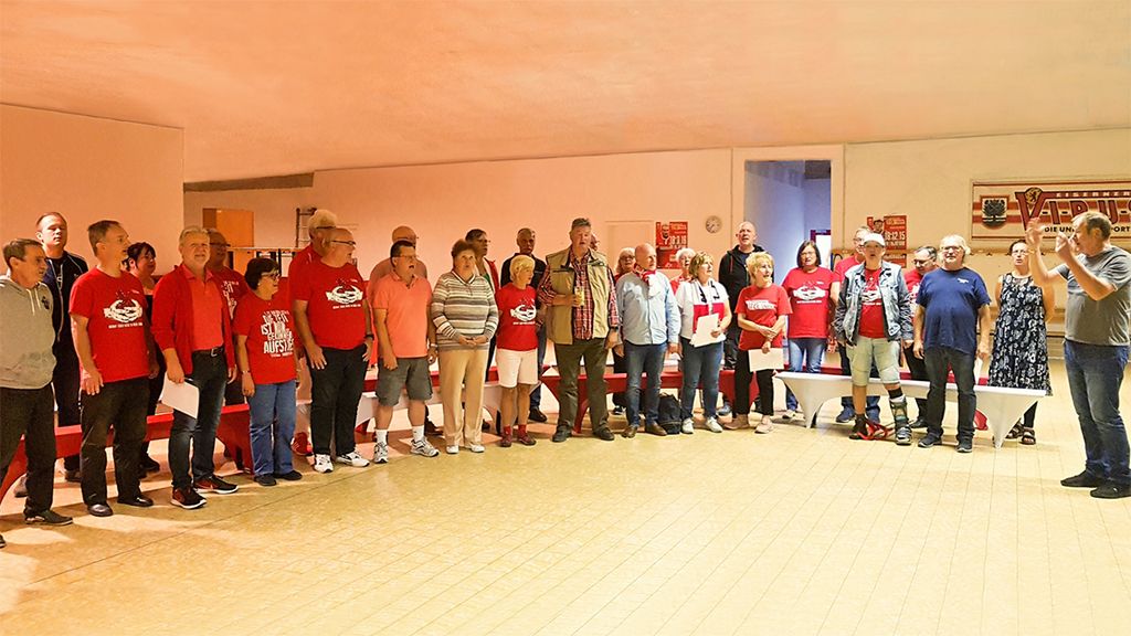 Eine Gruppe von Menschen in roten und weißen T-Shirts steht zusammen in einem Raum, einige halten Papiere in der Hand.