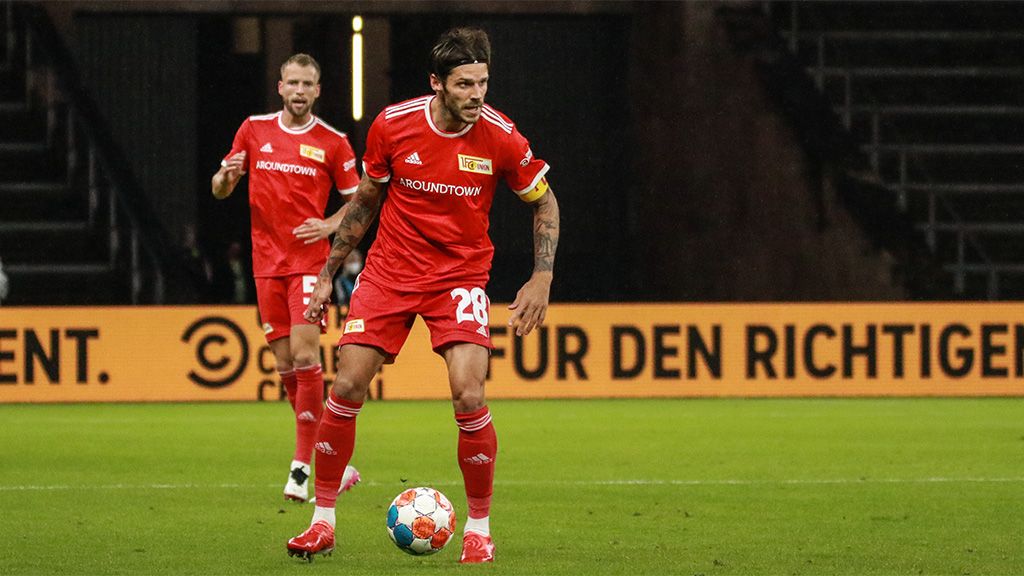 A soccer player in a red jersey with the number 28 is dribbling the ball while a teammate stands in the background.