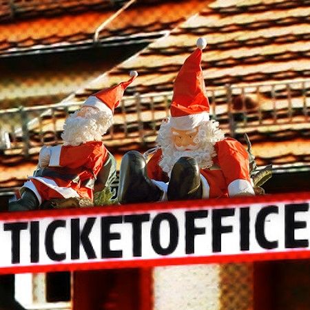 Zwei Weihnachtsmänner mit roten Hüten sitzen auf einem Dach über einem Schild mit der Aufschrift "TICKET OFFICE".