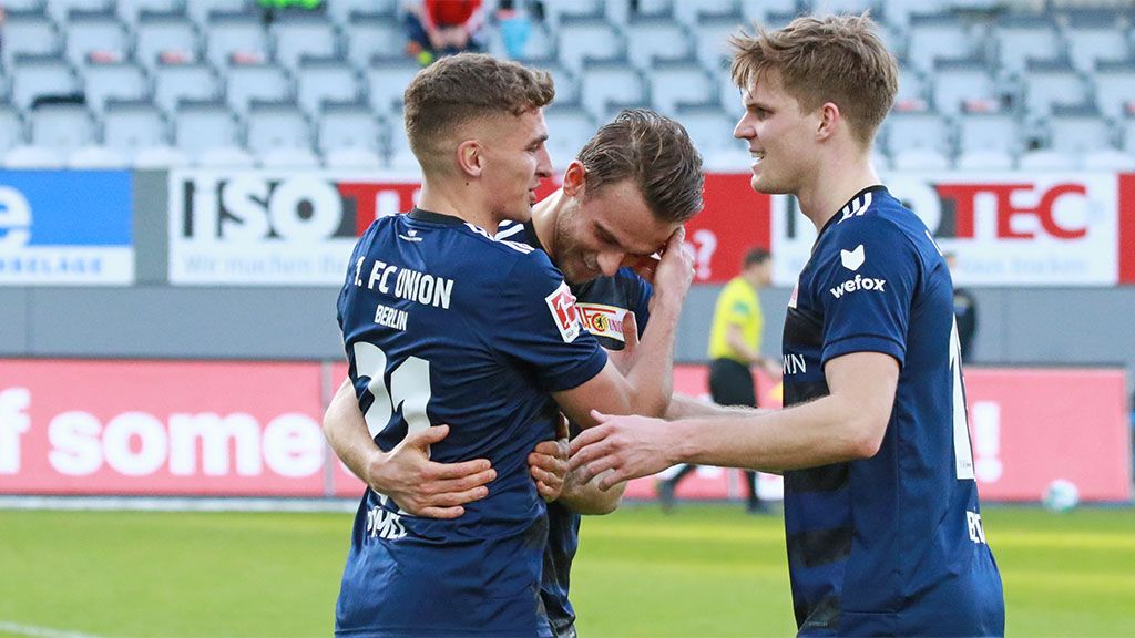 Three soccer players in blue jerseys celebrate a success on the field.