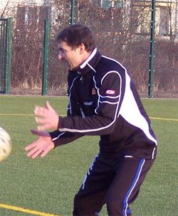 Ein Mann in sportlicher Kleidung steht auf einem Fußballfeld und bereitet sich darauf vor, einen Ball zu fangen.