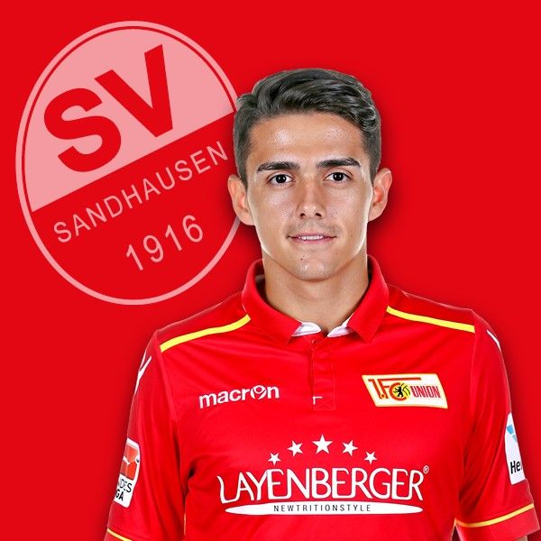 Ein junger Fußballspieler in rotem Vereinsdress mit dem Logo des SV Sandhausen im Hintergrund.