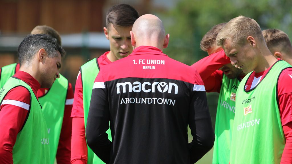 Eine Gruppe von Fußballspielern in Trainingskleidung bespricht sich, während einer Trainer im Vordergrund steht.