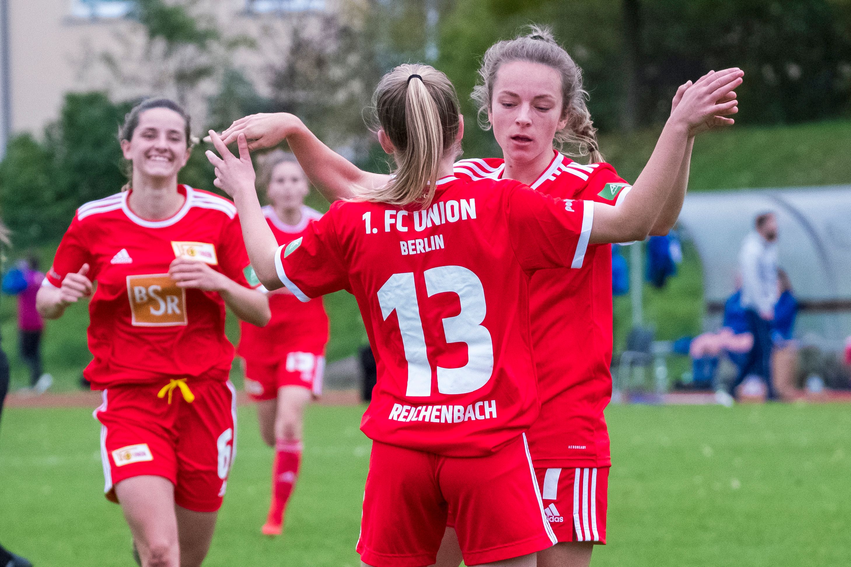 Zwei Spielerinnen vom 1. FC Union Berlin freuen sich über ein Tor. Eine andere Spielerin lächelt im Hintergrund.