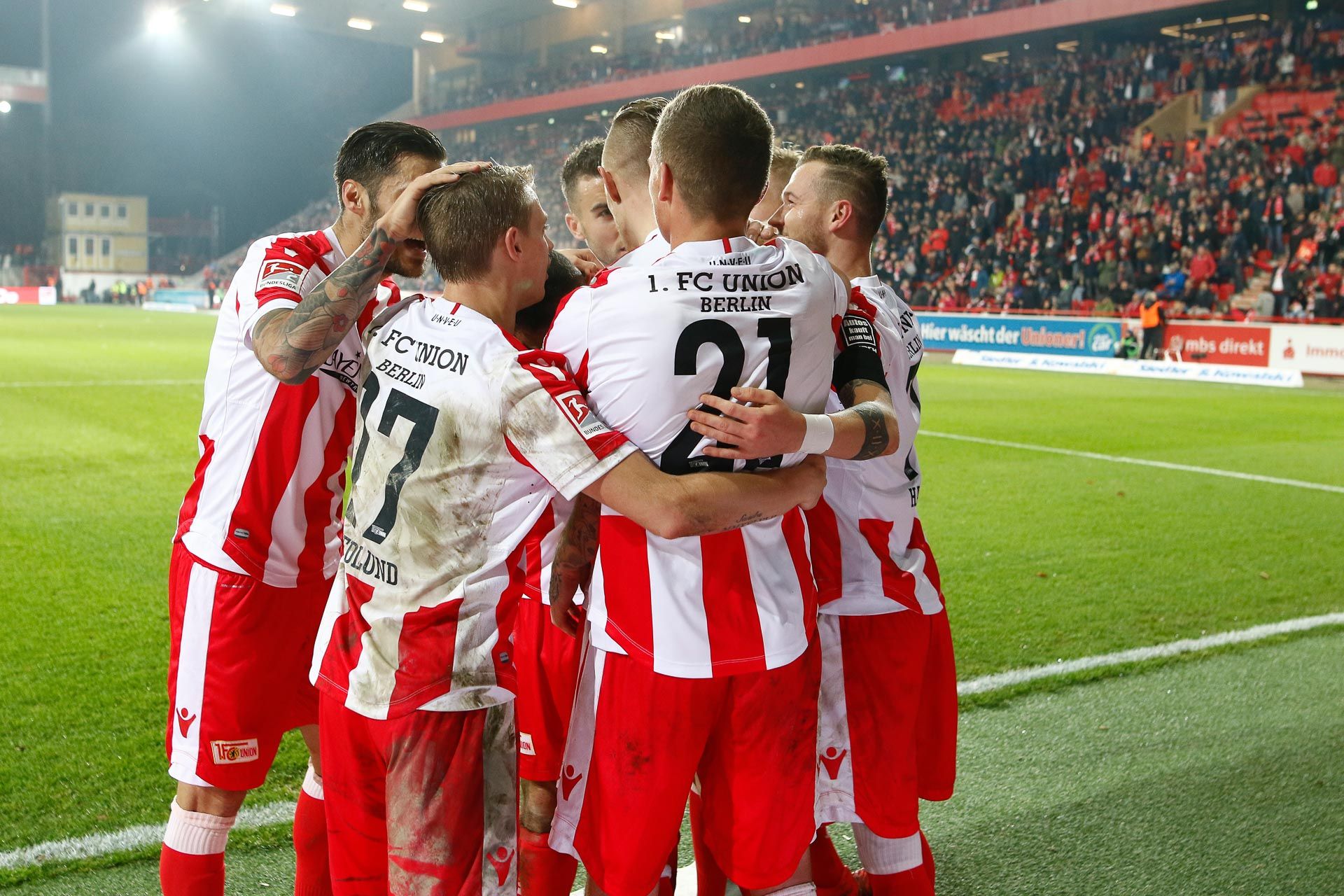 Die Spieler von 1. FC Union Berlin feiern. Sie haben ein Tor geschossen. Viele Fans sind im Stadion.