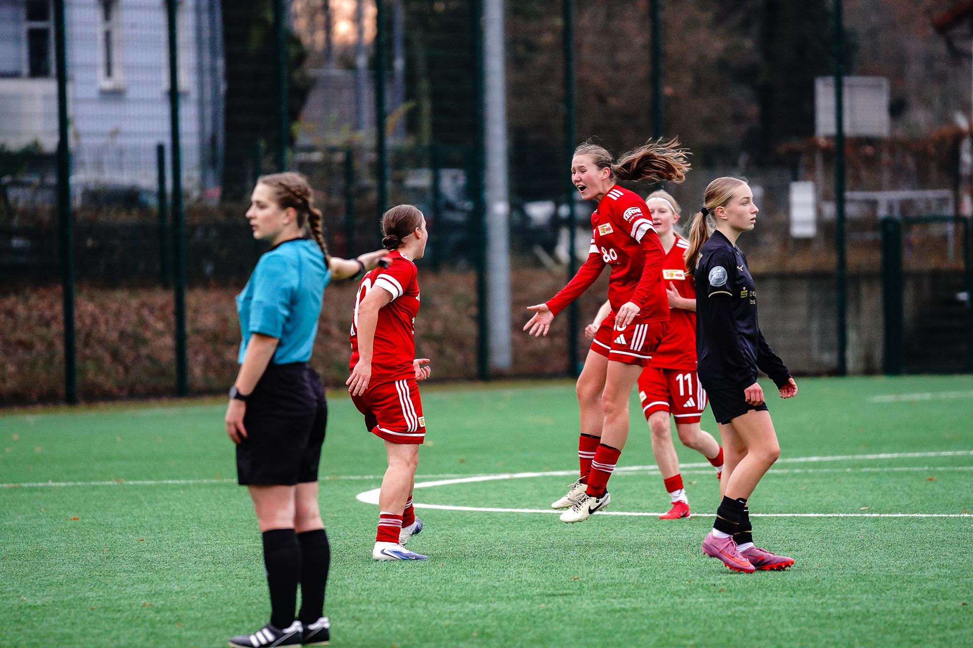 Zwei Spielerinnen des FC Union Berlin feiern ein Tor auf einem Fußballplatz, während eine Schiedsrichterin und eine Gegnerin zuschauen.