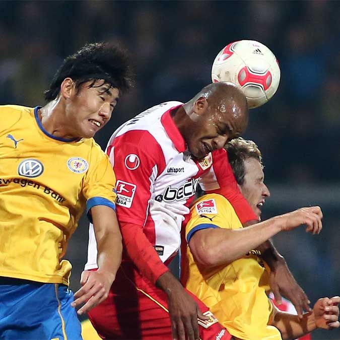 Zwei Fußballspieler kämpfen um den Ball, während einer von ihnen mit dem Kopf auf den Ball zielt.