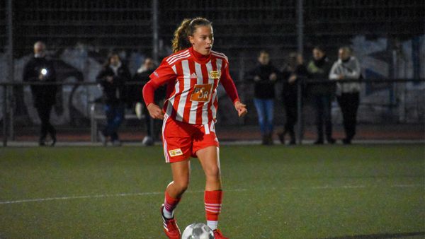 A soccer player in red-striped sportswear is dribbling the ball on a field surrounded by spectators.