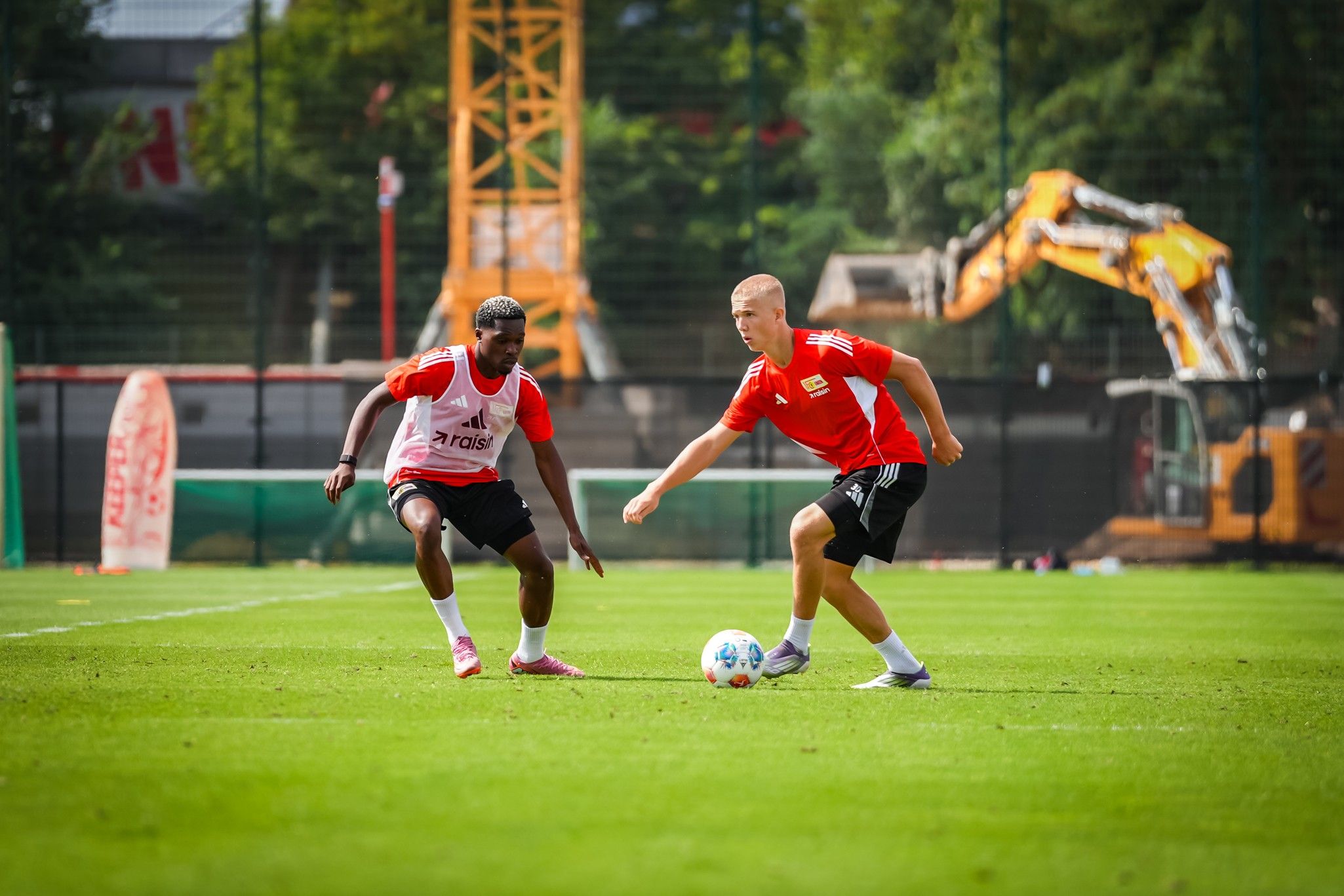 Zwei Fußballspieler trainieren auf einem grünen Sportplatz, während sie den Ball im Spielängern austauschen.