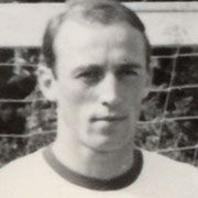 Schwarz-weiß-Foto eines männlichen Fußballspielers mit kurzem Haar, in einem sportlichen Oberteil vor einem Tor.