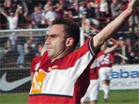 Ein Fußballspieler jubelt mit erhobenen Armen im Stadion, während die Zuschauer feiern.