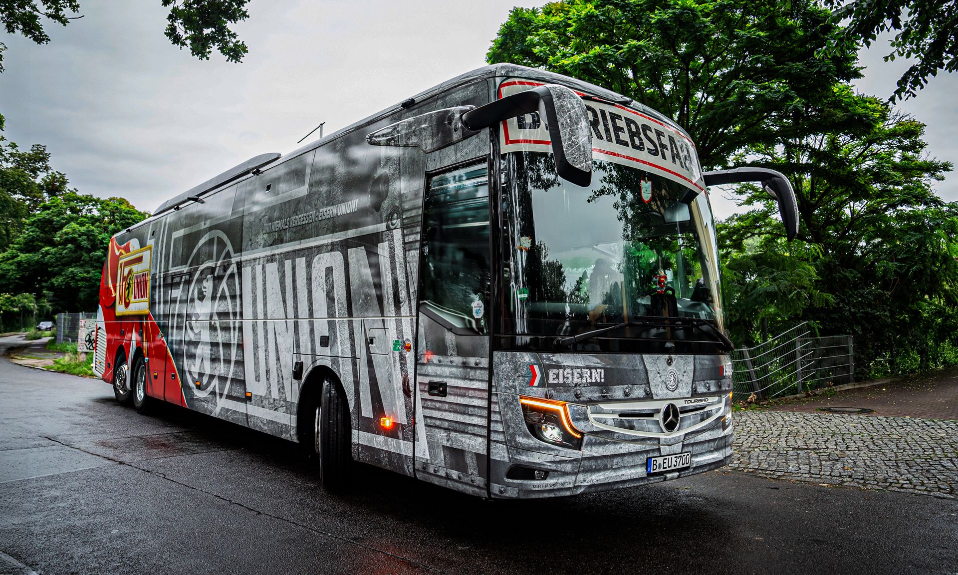 Ein Bus mit einem auffälligen Design, der im Freien steht, umgeben von grünen Bäumen und einem grauen Himmel.