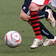 Nahaufnahme von zwei Fußballspielern, die in einer Aktion um den Ball kämpfen, mit Fokus auf deren Beine und die Fußballschuhe.