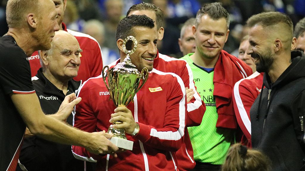 Eine Gruppe von Sportlern jubelt und hält einen Pokal in der Mitte, während sie sich lächeln und umarmen.