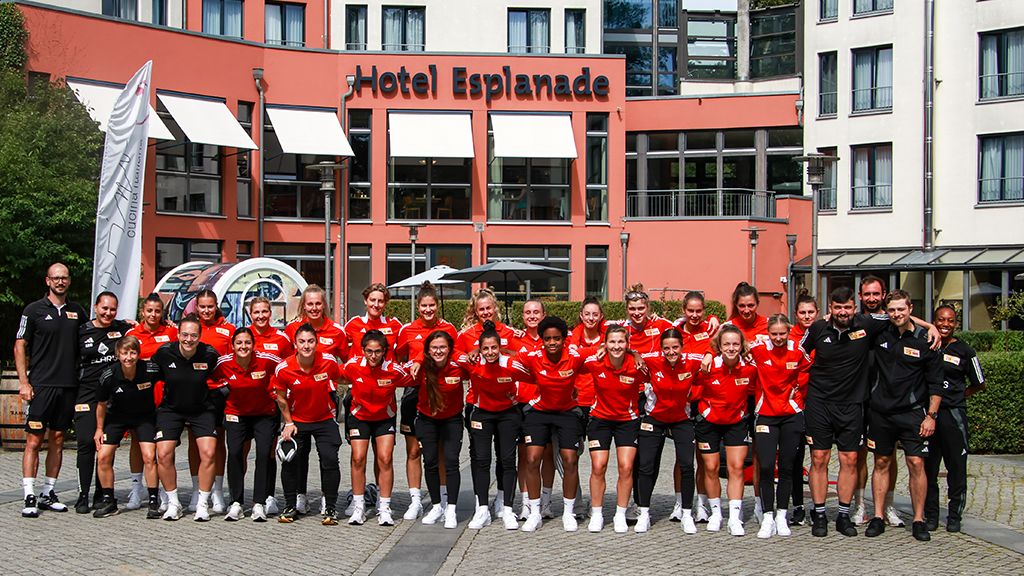 A group of athletes in red jerseys is posing in front of the Hotel Esplanade.