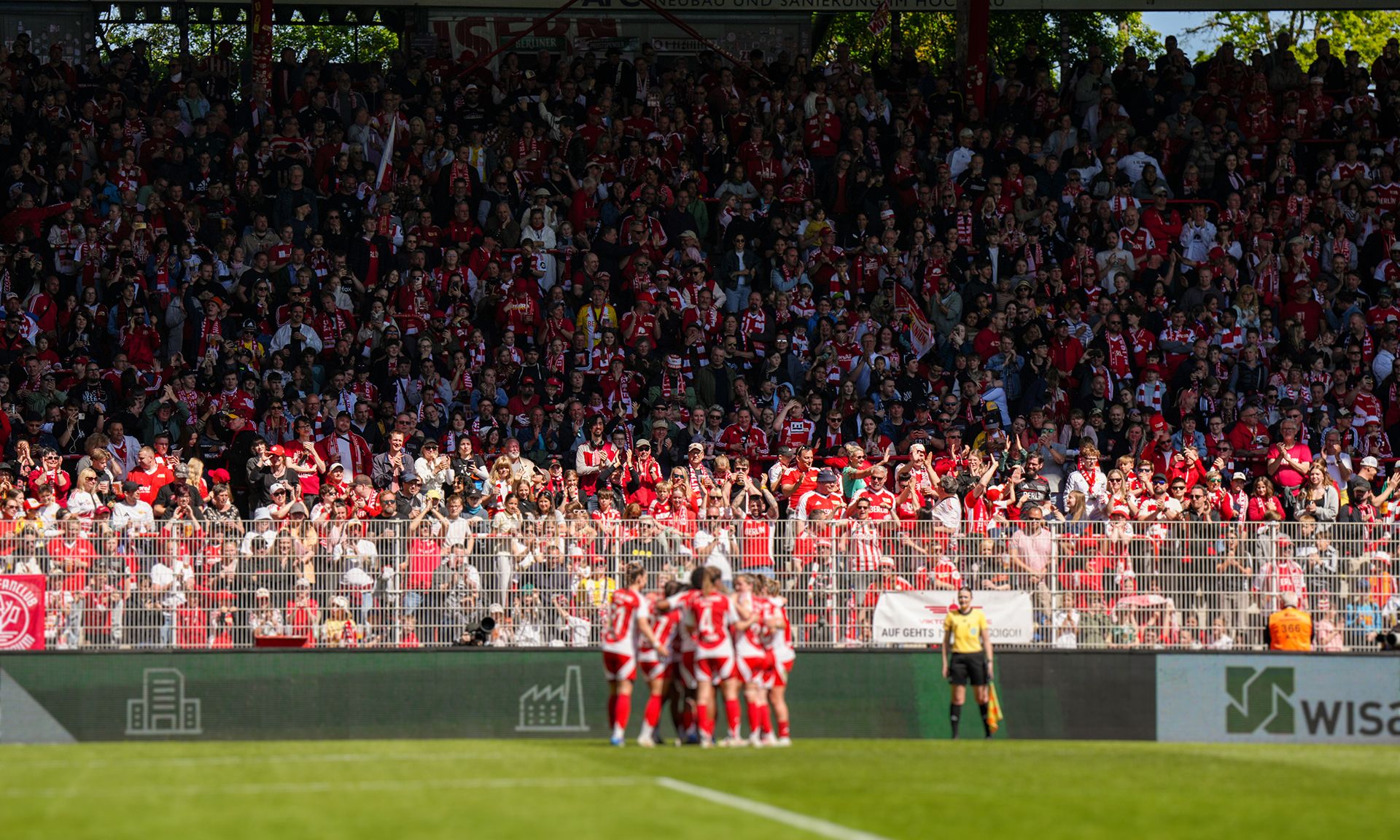 Fußballspiel: Eine jubelnde Menge in rot-weißen Trikots, Spieler feiern einen Torerfolg auf dem Platz.