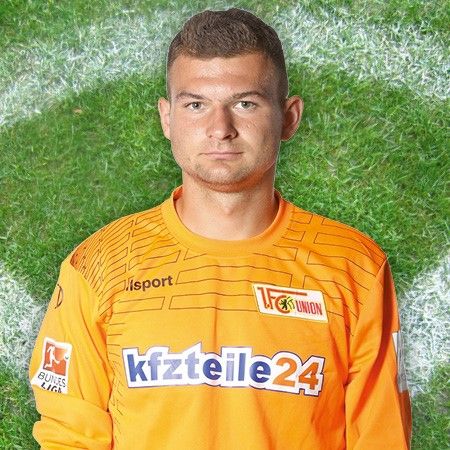 Der Alt-Text für das Bild lautet: „Fußballtorwart in orangefarbenem Trikot vor einem Rasenhintergrund.“