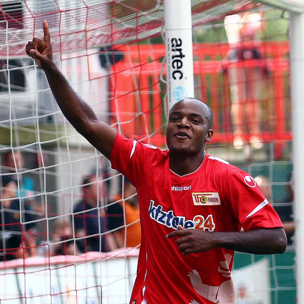 Ein Fußballspieler in rotem Trikot jubelt nach einem Tor, hebt den Finger und steht auf dem Spielfeld.