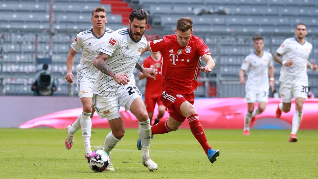 Zwei Fußballspieler verfolgen sich auf dem Spielfeld, ein Spieler trägt rote Uniform, der andere weiß-gestreifte.