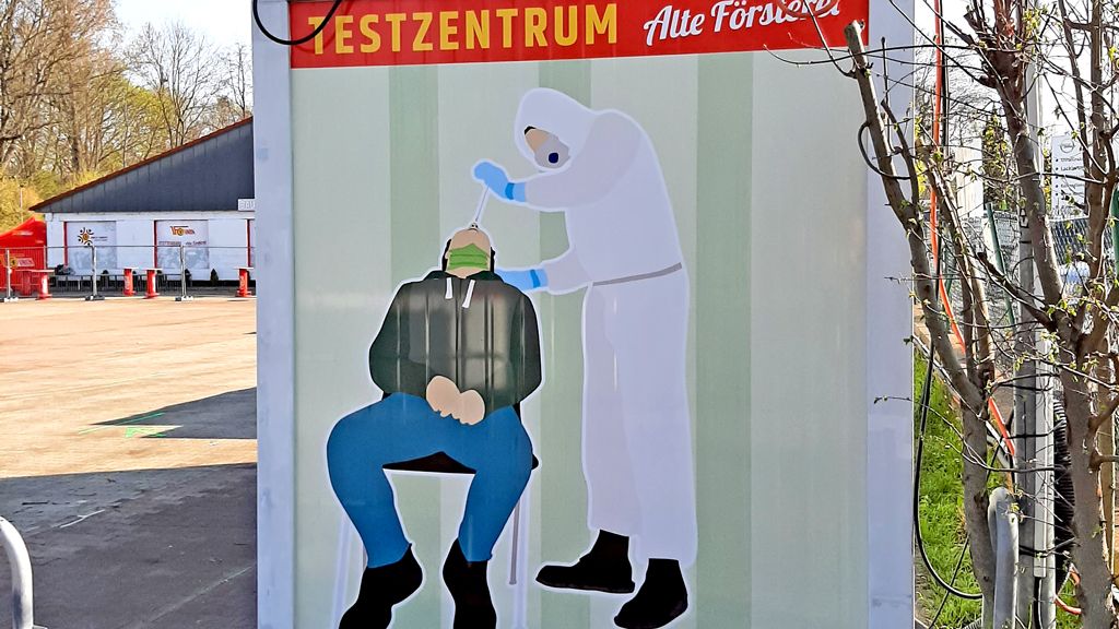 Ein Wandbild zeigt eine Person in Schutzkleidung, die eine andere Person auf einem Stuhl behandelt. Hintergrund mit Grün- und Grautönen.