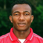 Ein Mann mit kurzem, schwarzem Haar, der ein rotes Sporttrikot trägt, blickt direkt in die Kamera vor einem grünen Hintergrund.