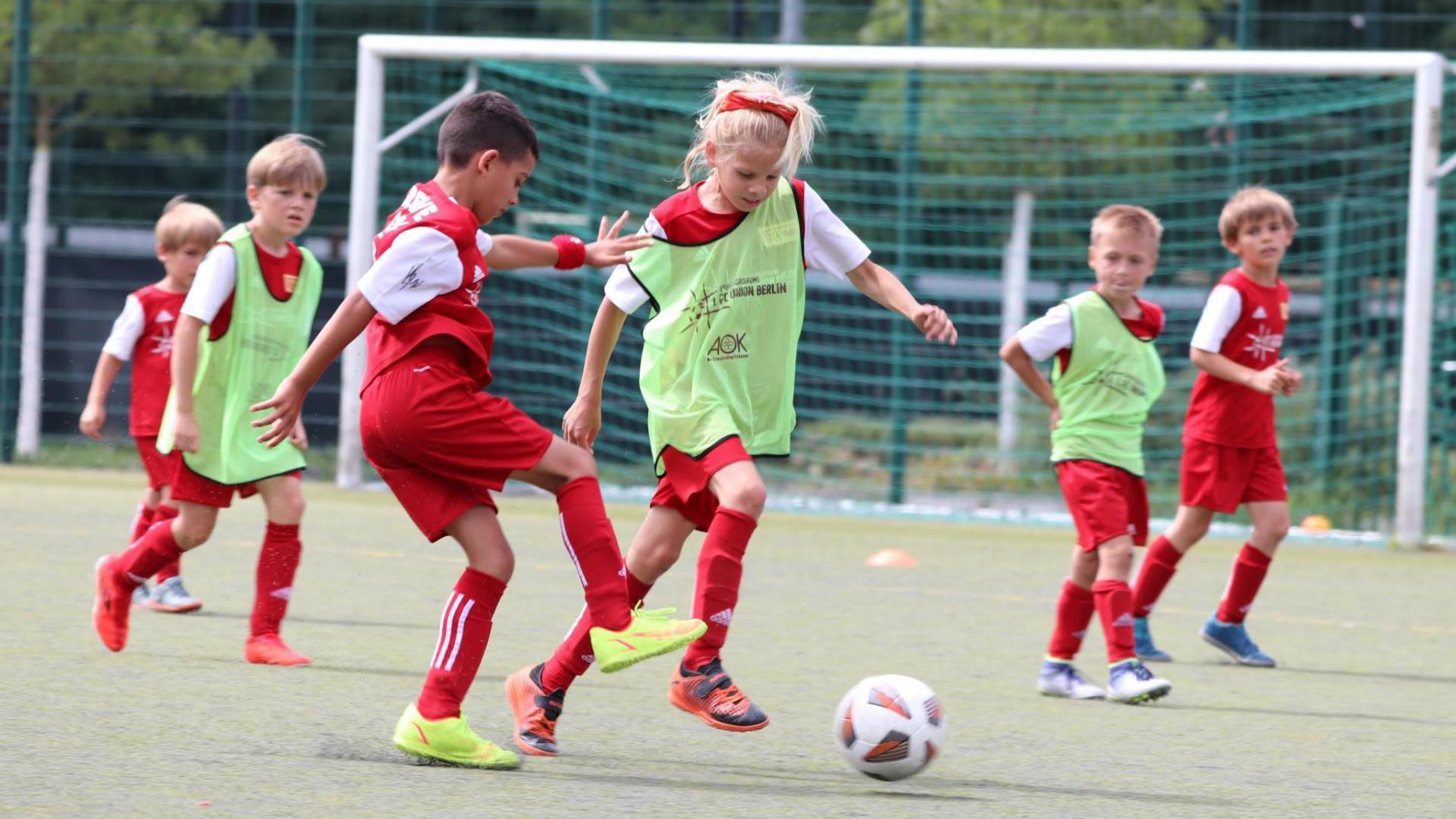 Kinder in roten Fußballtrikots trainieren auf einem Platz, während ein Junge den Ball dribbelt.