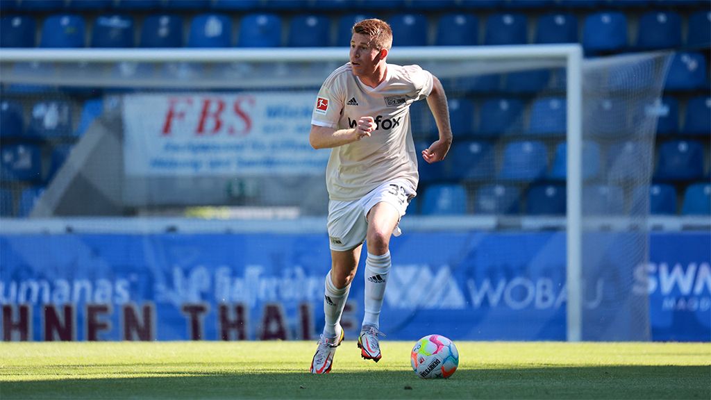 A soccer player sprints on the field, with a goal post visible in the background.