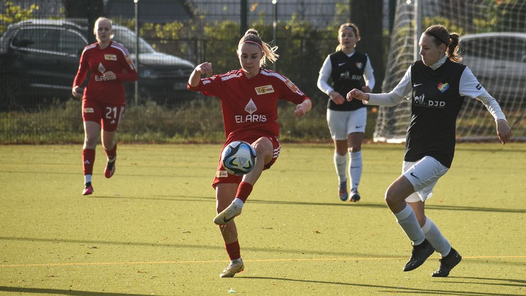 Zwei Frauenfußballerinnen spielen auf einem Kunstrasenplatz, eine führt den Ball, während eine andere sie verteidigt.