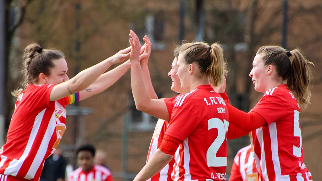 Four female soccer players in red jerseys celebrate a success on the field together.